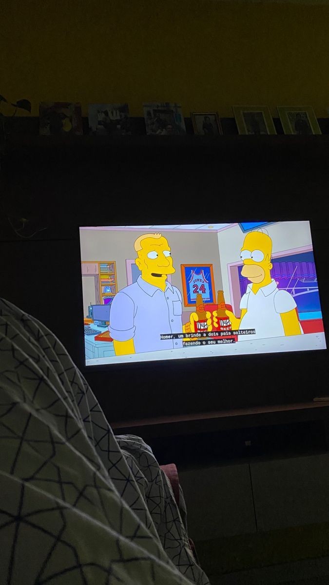 Person watching The Simpsons on a TV, showing two characters holding beer bottles with subtitles in Portuguese.